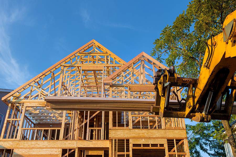 Heavy boom truck machinery is used to add the roof trusses to a timber frame house extension